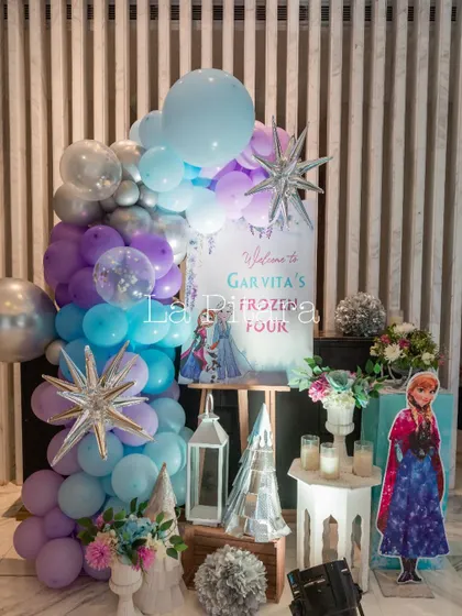 A welcome display for Garvita's 'Frozen Four' birthday, featuring a character cutout of Anna, themed signage, and a beautiful balloon arrangement in purple, blue, and silver.