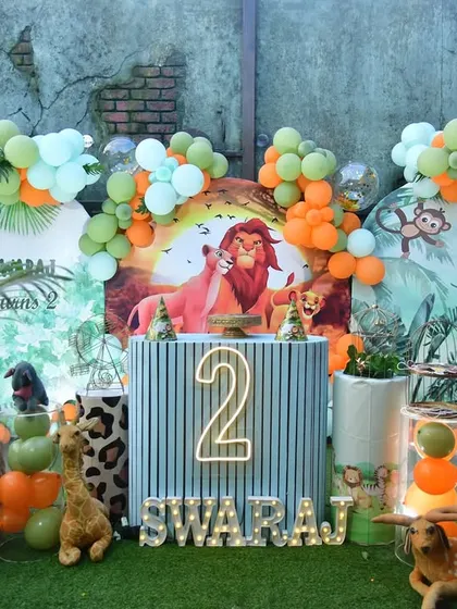 A Lion King themed party with a beautiful backdrop of Pride Rock. The setup includes plush animal toys and a neon number '2'.