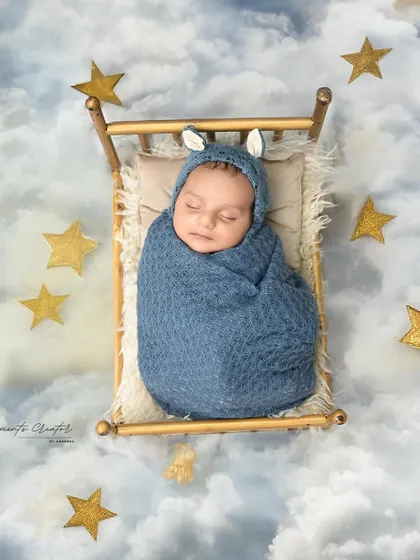 Dreaming among the stars. This newborn, wearing a cute bunny-eared cap, is nestled in a tiny bed that seems to float on a cloud-filled, starry sky.