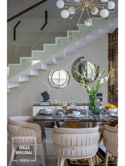 In this duplex home in Gujarat, the dining area is set against a modern staircase with a glass railing. The design uses sculptural chairs and a statement chandelier to create an elegant dining experience.
