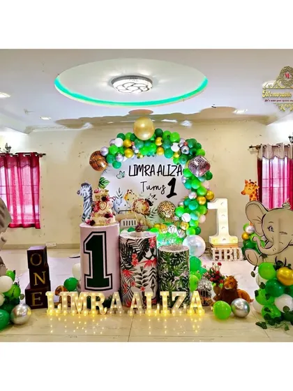 A jungle-themed first birthday party with elephant cutouts and a green and gold balloon arrangement.