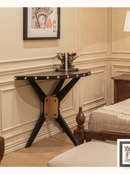 This wooden console table blends artisanal woodworking with a touch of industrial design. The dark wood top with brass-studded details and the crossed-leg base create a unique and characterful piece.
