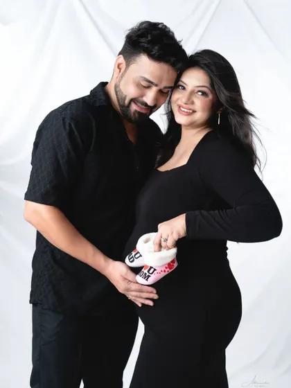 A sweet detail shot. The couple holds a pair of "I love Mom" and "I love Dad" baby shoes over the bump, a perfect prop for any maternity shoot.