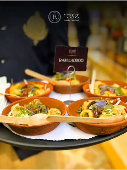 A server presents a tray of Ram Laddoos, a popular Delhi street food snack. We serve these savory lentil fritters in traditional terracotta bowls, garnished and ready to eat.