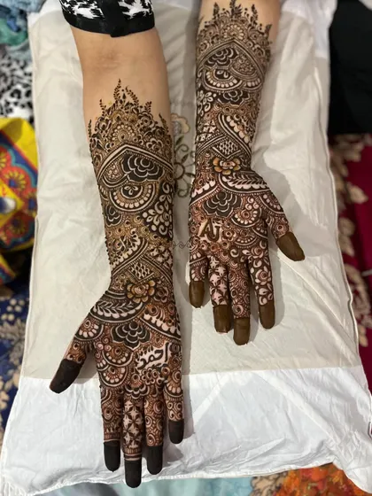 Full view of an intricate engagement henna design. The pattern features symmetrical heart shapes and detailed floral work extending up the arms.