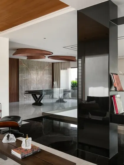 A family lounge in the Timber Edge project, where a glossy black partition doubles as a bookshelf. The space is unified by black marble flooring and a slatted timber ceiling.