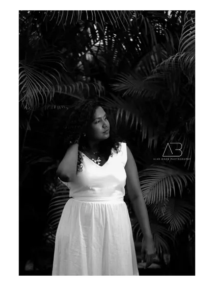 A classic black and white portrait against a backdrop of palm leaves. The contrast between her white dress and the dark leaves creates a striking composition.