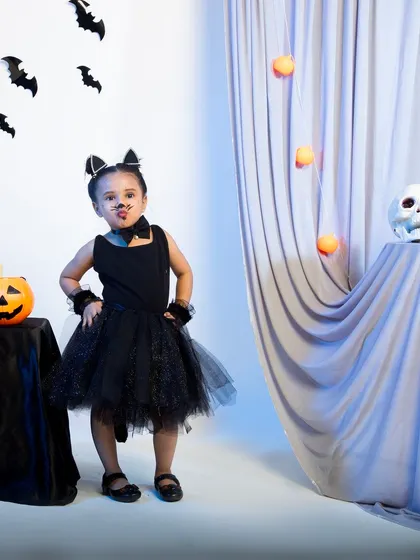A child in a black cat costume making a cute face for the camera.
