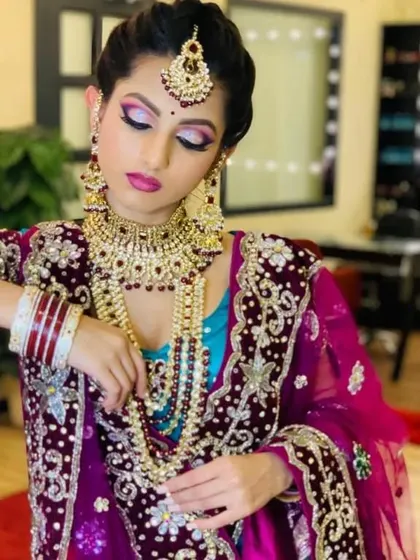 A North Indian bridal look featuring a stunning purple and blue lehenga with intricate embroidery. The makeup is glamorous with a focus on the eyes.