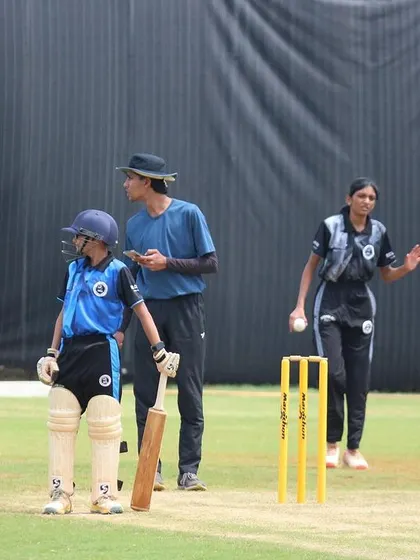 A young bowler delivers the ball during a practice match, with an umpire closely monitoring the game.