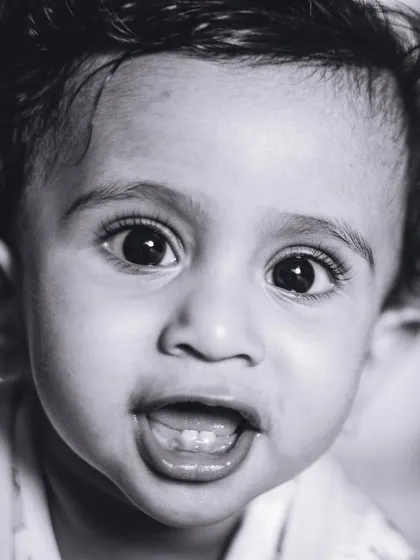 A striking black and white close-up of a baby's face, highlighting their bright eyes and first teeth.