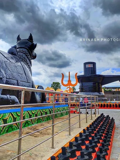 The impressive Nandi and Shivalinga statues at Kotilingeshwara temple stand under a dramatic, cloudy sky. This wide-angle shot captures the grandeur of the religious site in Kolar.