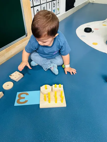 This child is sorting shapes and counting pegs, learning about numbers and quantities through a hands-on wooden toy.