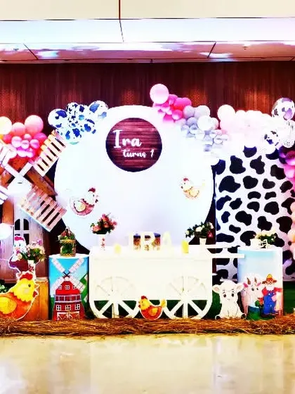 A charming farm animal theme for Ira's first birthday. The setup includes a classic red barn tractor, hay bales, and cute cutouts of sheep, pigs, and cows for a fun barnyard party.