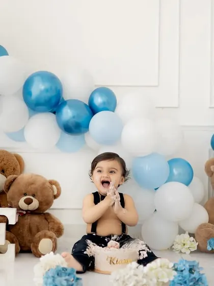 A classic teddy bear picnic cake smash. The blue and white balloon garland adds a festive touch to this adorable first birthday celebration.