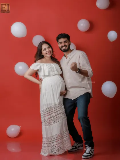 A fun and celebratory studio shot with a vibrant red background and white balloons. The couple's joyful energy is contagious.