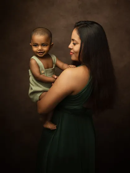 A mother gazes lovingly at her smiling baby. This fine art portrait, with its painterly background, beautifully captures a moment of pure connection.