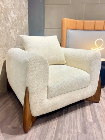 A single armchair in a white bouclé fabric with unique, fin-like wooden legs. This piece is a perfect example of how I blend natural materials with modern, sculptural forms.