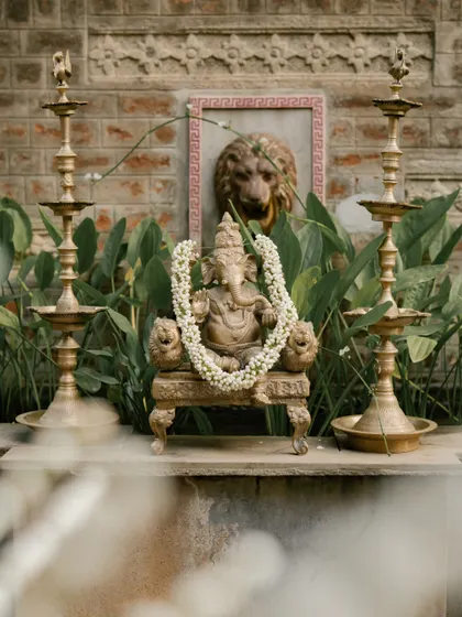 A Ganesha idol placed amidst greenery and traditional lamps, invoking blessings for the couple's new beginning.