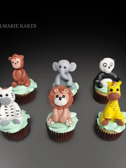 A set of adorable animal-themed cupcakes. Each cupcake is topped with a hand-sculpted fondant animal, including a lion, panda, giraffe, zebra, monkey, and elephant.