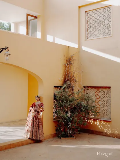 A majestic bridal portrait. The bride stands in a sun-drenched courtyard with beautiful architecture, looking like royalty.