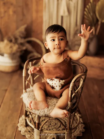 A playful wave from a little boy in a rattan chair. This shot perfectly captures the fun and interactive nature of a sitter session.
