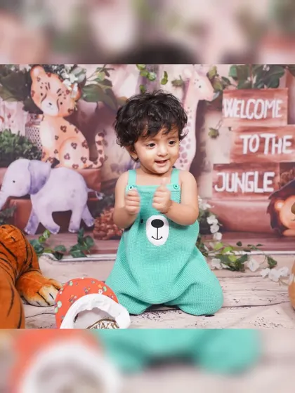 Welcome to the jungle! This little explorer is giving two thumbs up in our safari-themed studio setup, surrounded by plush animal toys and a wooden sign.