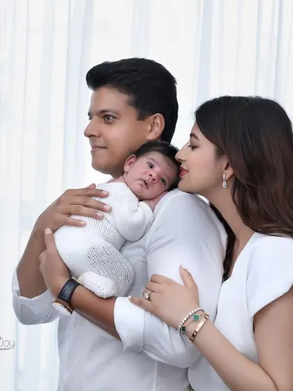 A candid family portrait where the mother leans in to kiss her partner while he holds their baby. This shot captures the love that fills the home with a new baby's arrival.