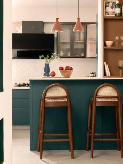 The kitchen is designed around a functional island that doubles as a breakfast bar. I chose a deep teal for the cabinetry and paired it with warm wood bar stools and terracotta pendant lights for a rich, layered look.