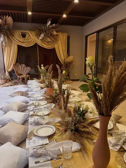 An intimate and chic boho-style gathering perfect for a relaxed celebration. This setup features low picnic tables, plush floor cushions, and earthy decor with pampas grass, creating a warm and inviting atmosphere for guests to connect and enjoy.