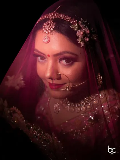 A stunning close-up portrait of the bride, her face partially veiled by a pink dupatta, creating a look of timeless grace.