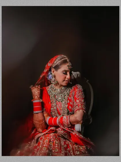A moody and artistic seated portrait of the bride. The soft, directional lighting highlights the texture of her lehenga and her contemplative expression.