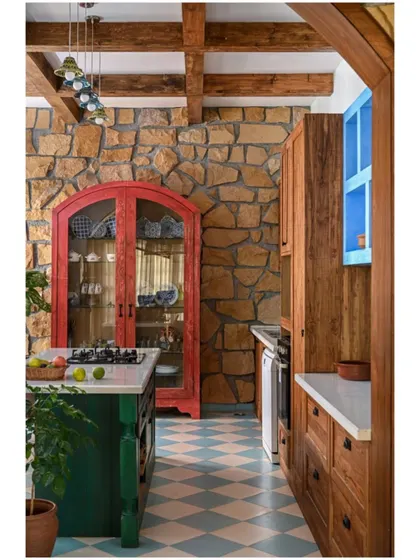 This kitchen is miles away from any current trend, with its bold color choices, natural stone wall, and mix of finishes.
