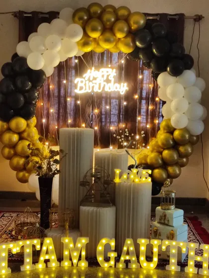A stylish birthday setup with a black, white, and gold balloon arch. The full prop display and marquee letters complete the look.