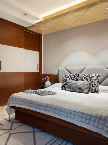 The master bedroom at Rue 32 redefines serenity with a refined palette of greys and blues. A commanding bed with a grey upholstered headboard lies beneath a herringbone wooden ceiling that adds rustic elegance.
