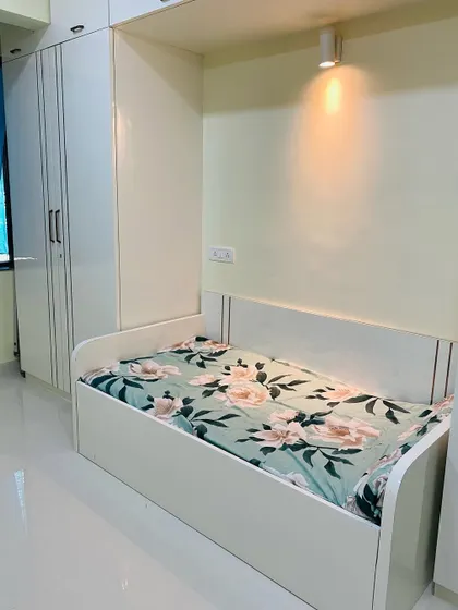 A compact bedroom design featuring a single bed with a built-in headboard and an attached wardrobe. A small wall-mounted light provides a cozy reading spot.