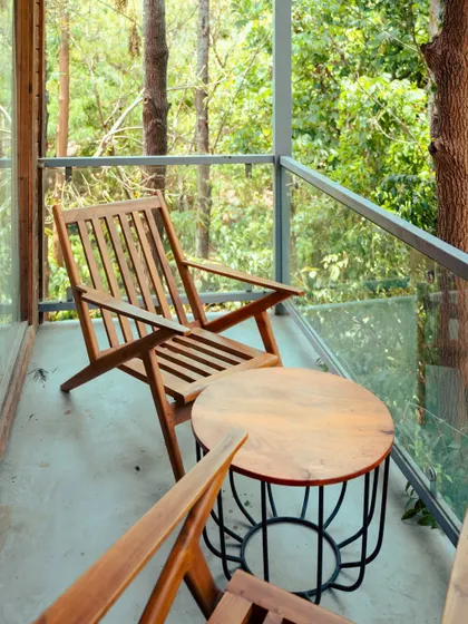 A quiet corner on a balcony, with a wooden chair and table overlooking the dense forest.