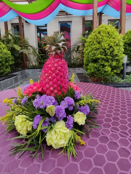 A unique table centerpiece featuring a pineapple painted pink and surrounded by a vibrant floral arrangement, perfectly matching the quirky and colorful theme.