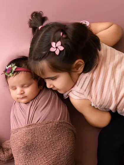 A sweet moment as an older sister leans in to look at her sleeping newborn sibling.