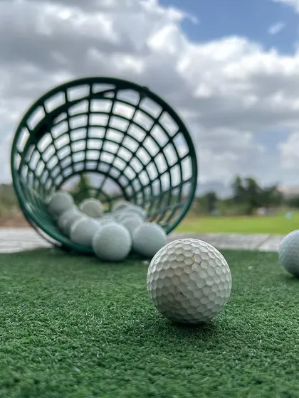 A close-up shot of golf balls on the practice mat, ready for a session. The dimpled texture of the ball in the foreground invites you to come and hit a few.