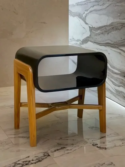 The "Plain Jane" side table offers immaculate mid-century vibes. Its sleek black gloss top with a rounded, open-shelf design sits on a solid teak wood base, making it a stylish and functional piece of accent furniture.