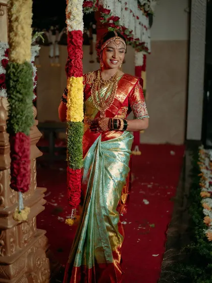 A full-length shot of bride Bhushitha at her Muhurtham. The vibrant colors of the decor and her saree are perfectly balanced with a classic, radiant makeup look.