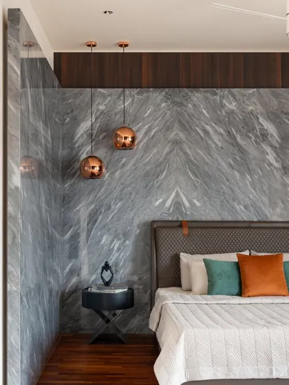A guest bedroom featuring a book-matched marble wall as a dramatic headboard. Copper-toned pendant lights add a warm, metallic accent.