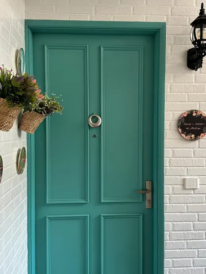 A closer view of the teal door, highlighting its classic paneling and the rustic charm of the surrounding white brick wall and vintage-style lantern.