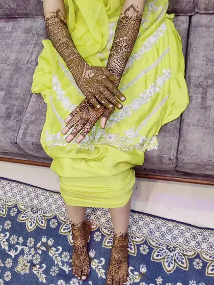 A beautiful bride showing her full mehndi work. The designs extend up the arms and include delicate patterns on the feet for a complete and traditional look.