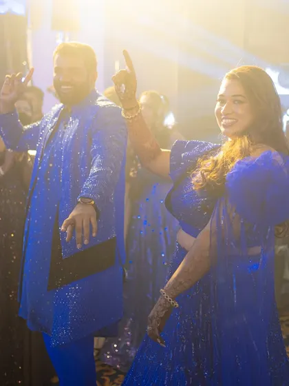 The couple enjoying their sangeet night, dancing together. Their coordinated royal blue outfits sparkle under the stage lights, making them the center of attention.