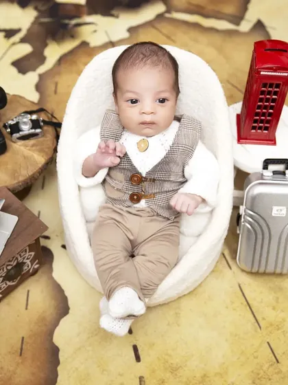 A different perspective of the "Boss Baby" travel theme, showing the full setup with a world map backdrop. The awake baby is posed in a comfortable chair, surrounded by travel-related props.