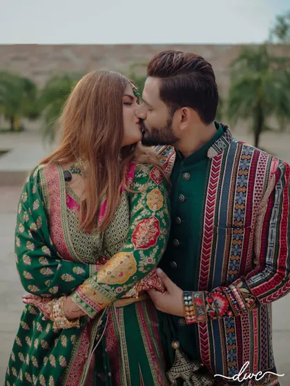 A passionate kiss shared by the couple, their vibrant green and multi-colored outfits adding to the richness of the moment.