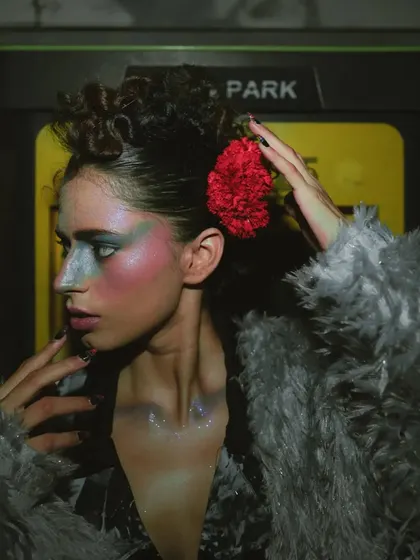 A close-up from 'Lampione', focusing on the dramatic, multi-colored makeup and floral hair accessory.