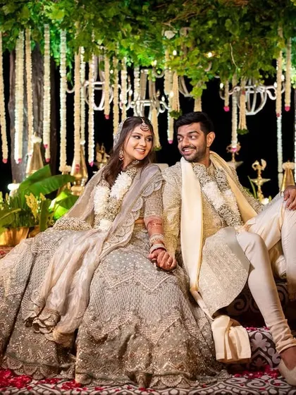 A beautiful portrait of a couple on their wedding stage, which features a canopy of hanging white floral strings and elegant chandeliers, creating a serene and luxurious atmosphere.